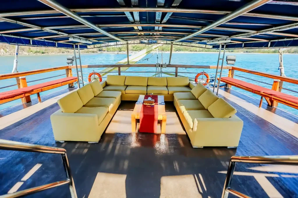 Shaded sun deck of a phinisi liveaboard with lounge seating and open sea beyond